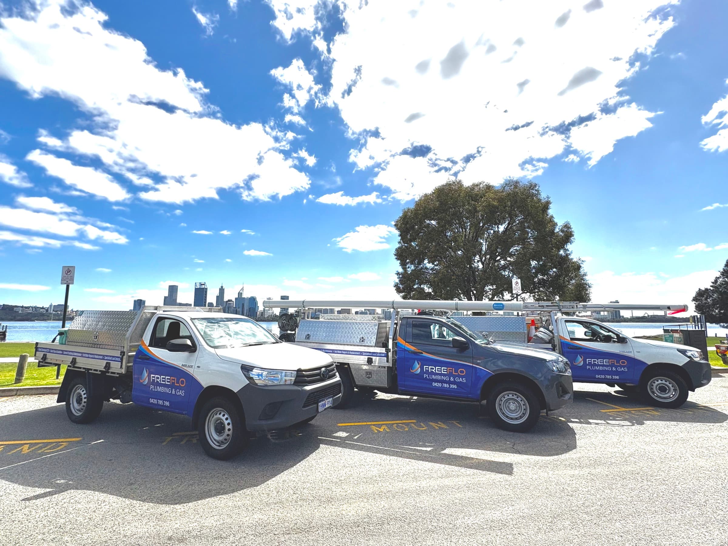 FreeFlo Plumbing & Gas utes parked on the Swan River foreshore with the Perth city skyline behind