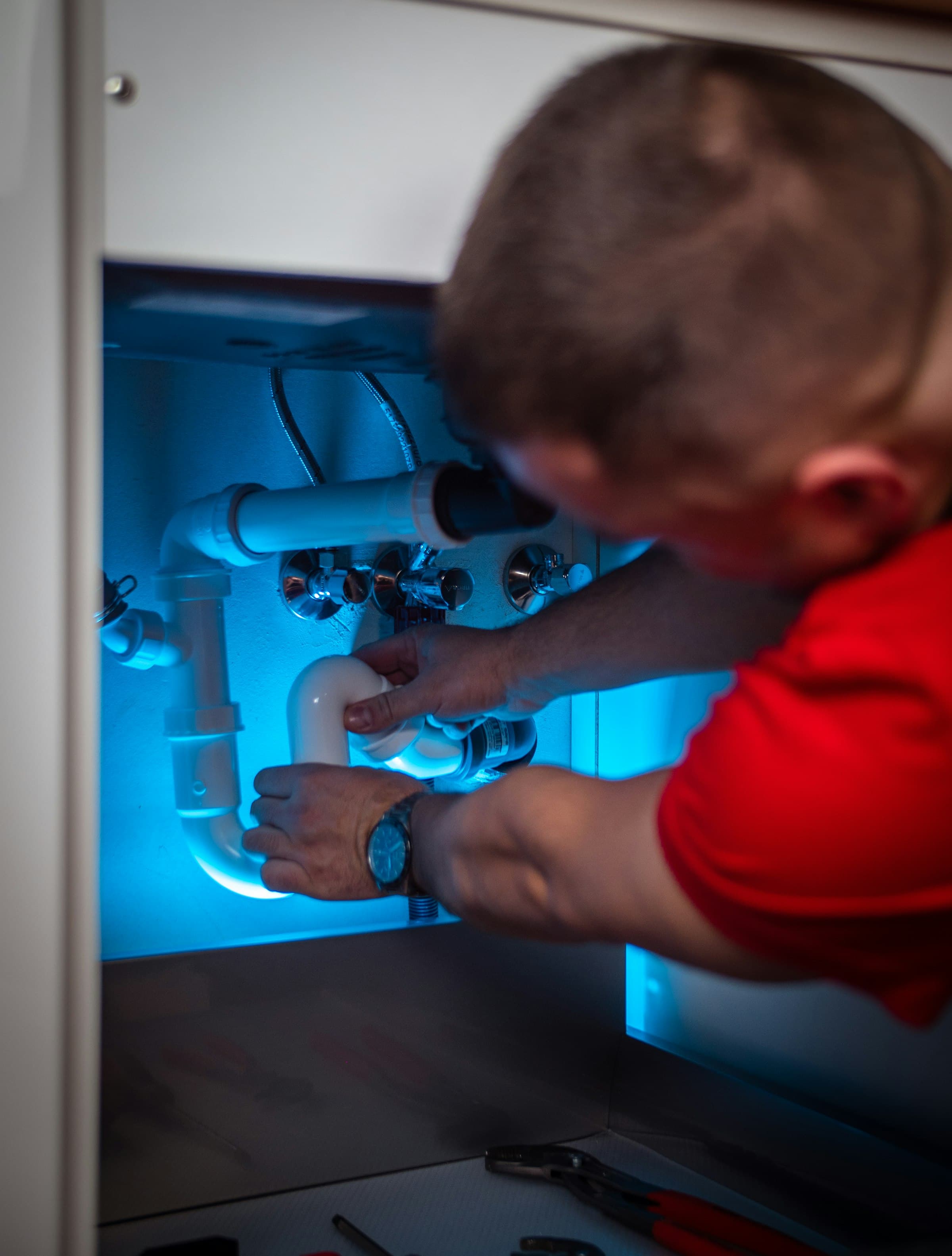 A plumber working on pipework inside a cabinet